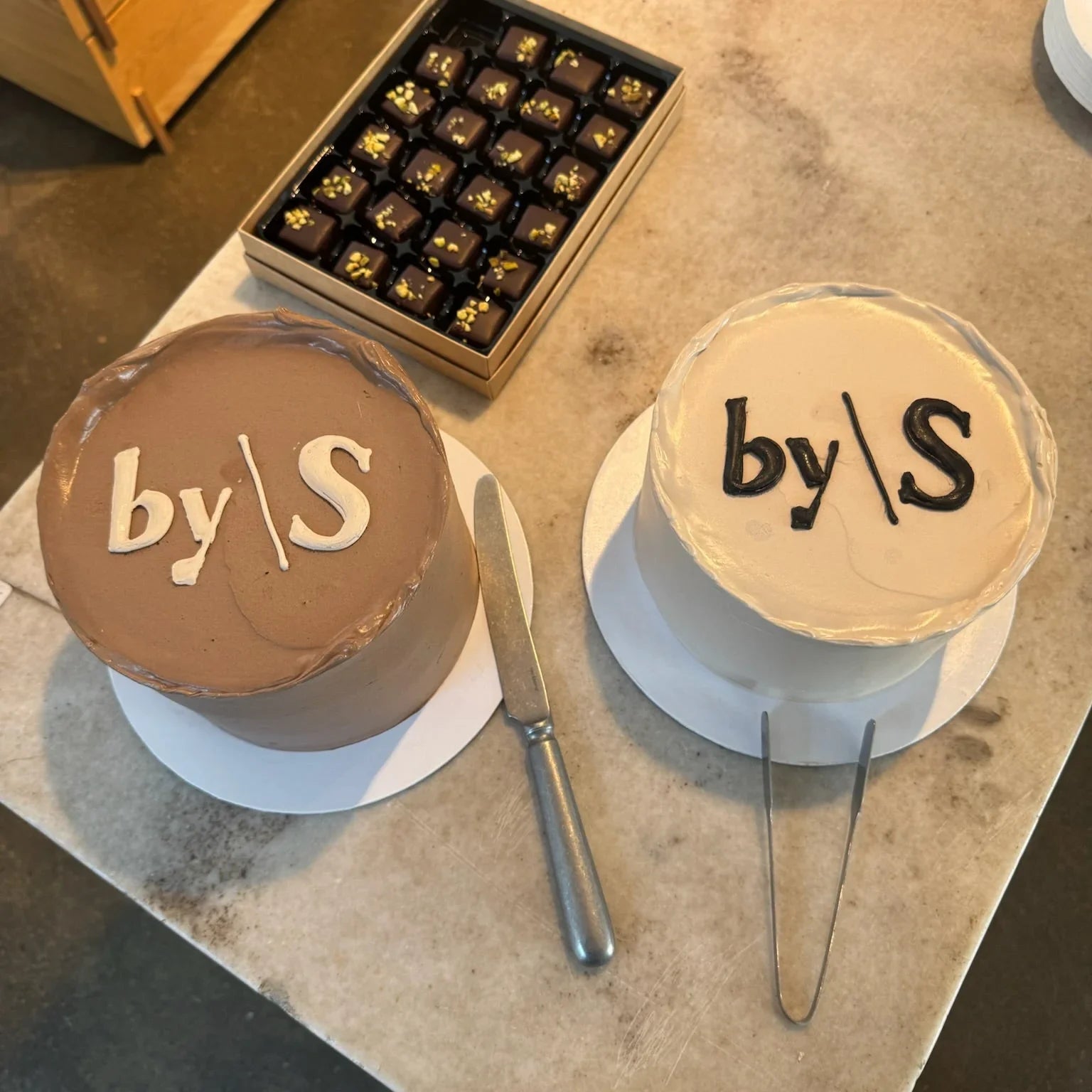 Two cakes with 'by S' branding on a table.
