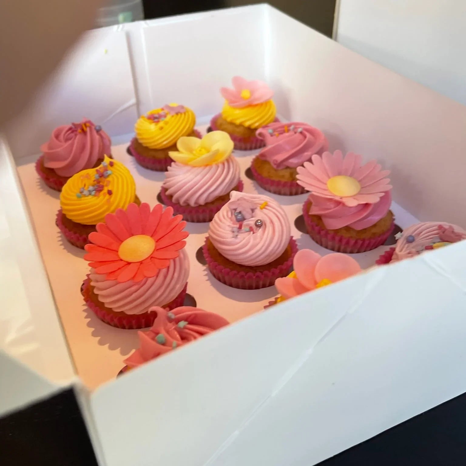 Decorative cupcakes with pink, yellow, and orange frosting in a box.
