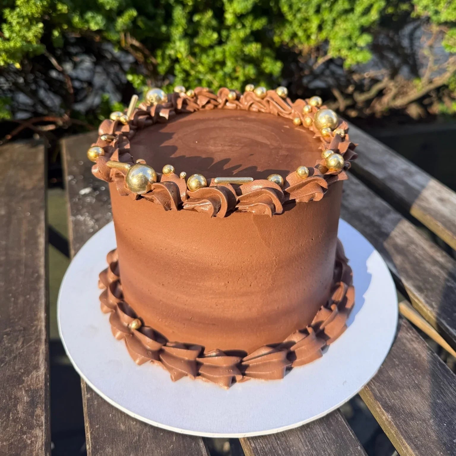 Chocolate cake with gold decorations on a wooden table outdoors
