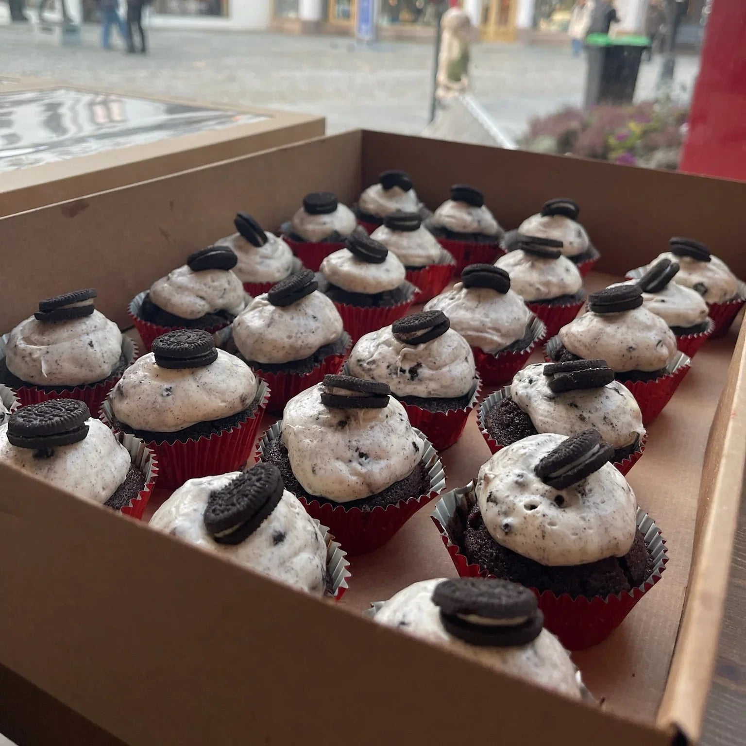 Box of cupcakes with Oreo toppings on a city street background
