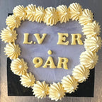 Decorative cake with yellow icing letters spelling "L.V ER 9 ÅR" on a gray background