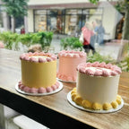 Three mini cakes with pink and yellow icing on a wooden table outdoors.