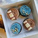 Four cupcakes with blue and brown frosting in a box on a wooden surface.