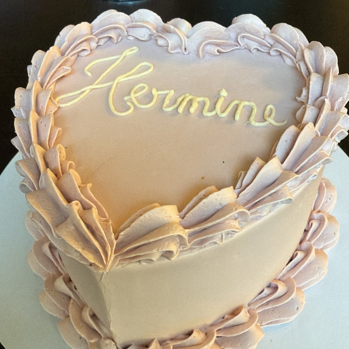 Heart-shaped cake with 'Hermine' written on it, surrounded by decorative elements.