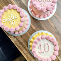 Three birthday cakes with pink and yellow icing on a wooden surface
