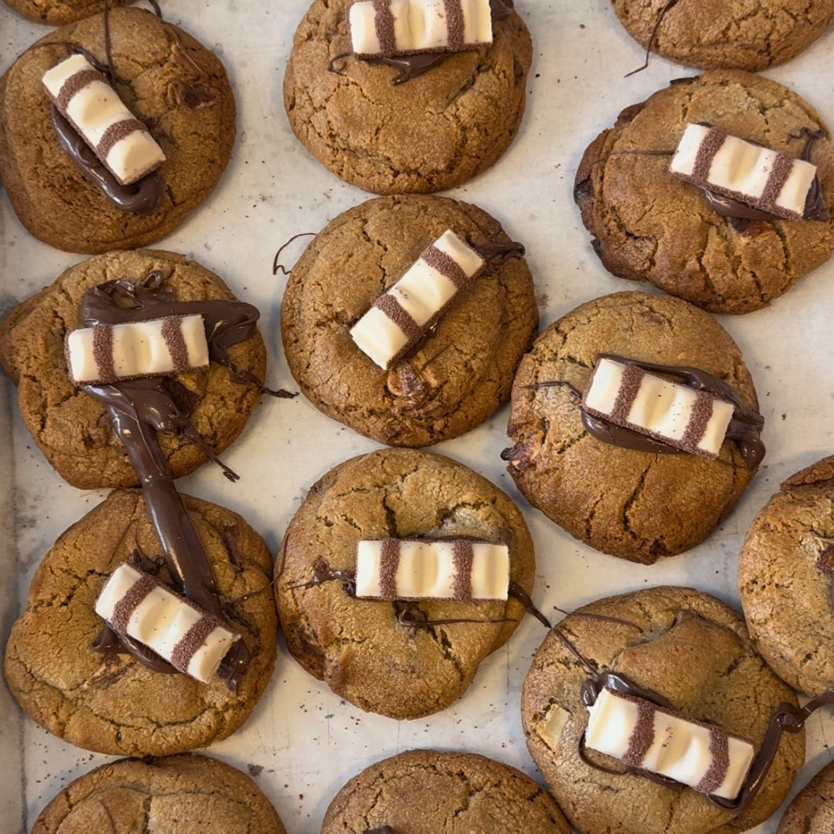 Cookies with chocolate and kinder bars arranged on a baking sheet.