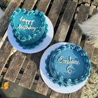 Two custom blue birthday cakes on a wooden table.