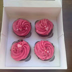 Four cupcakes with pink frosting in a box on a wooden surface