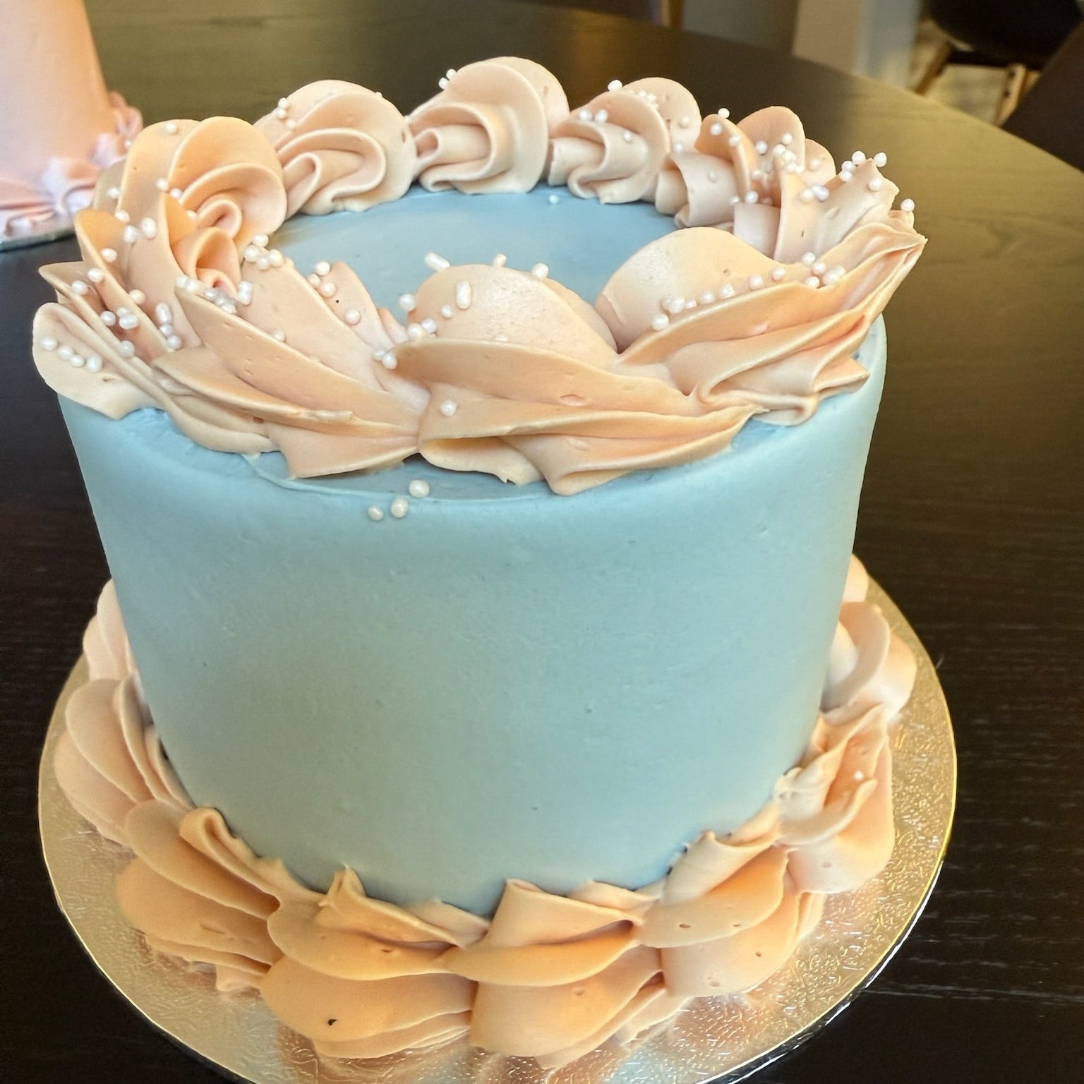 Blue mini cake with beige floral decorations on a dark surface