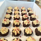 Mini chocolate cupcakes with white frosting and red sprinkles arranged in a box.