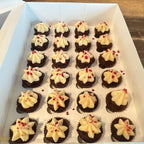 Mini chocolate cupcakes with white frosting and red sprinkles arranged in a box.