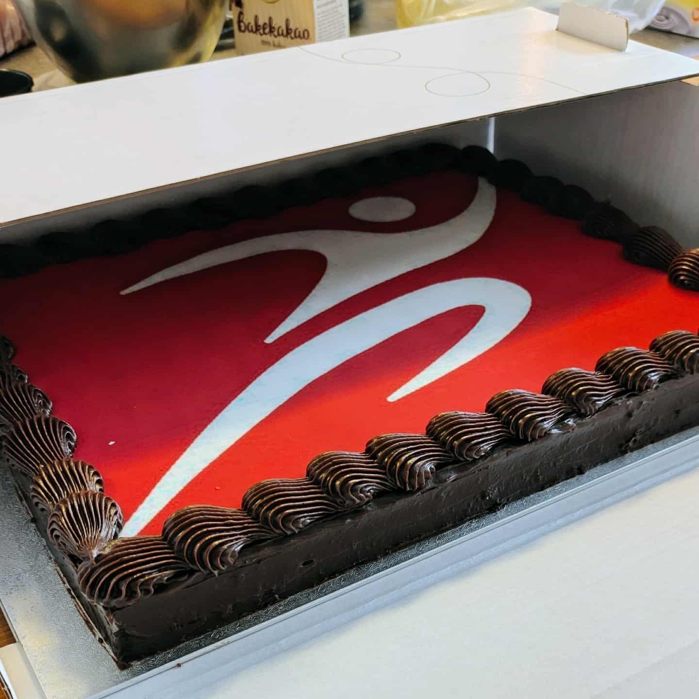 Chocolate cake with a red and white logo on top, likely a brand logo, in a box.