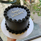 Black birthday cake with 'happy birthday' text held by a person indoors.
